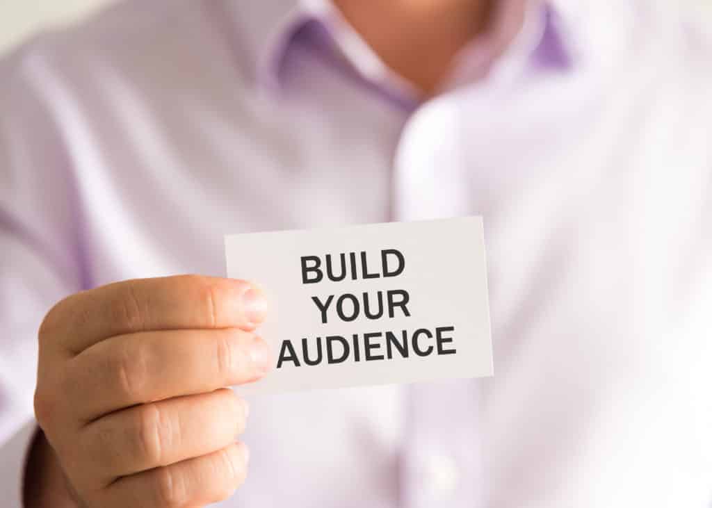 A man holding a card that says "build your audience"