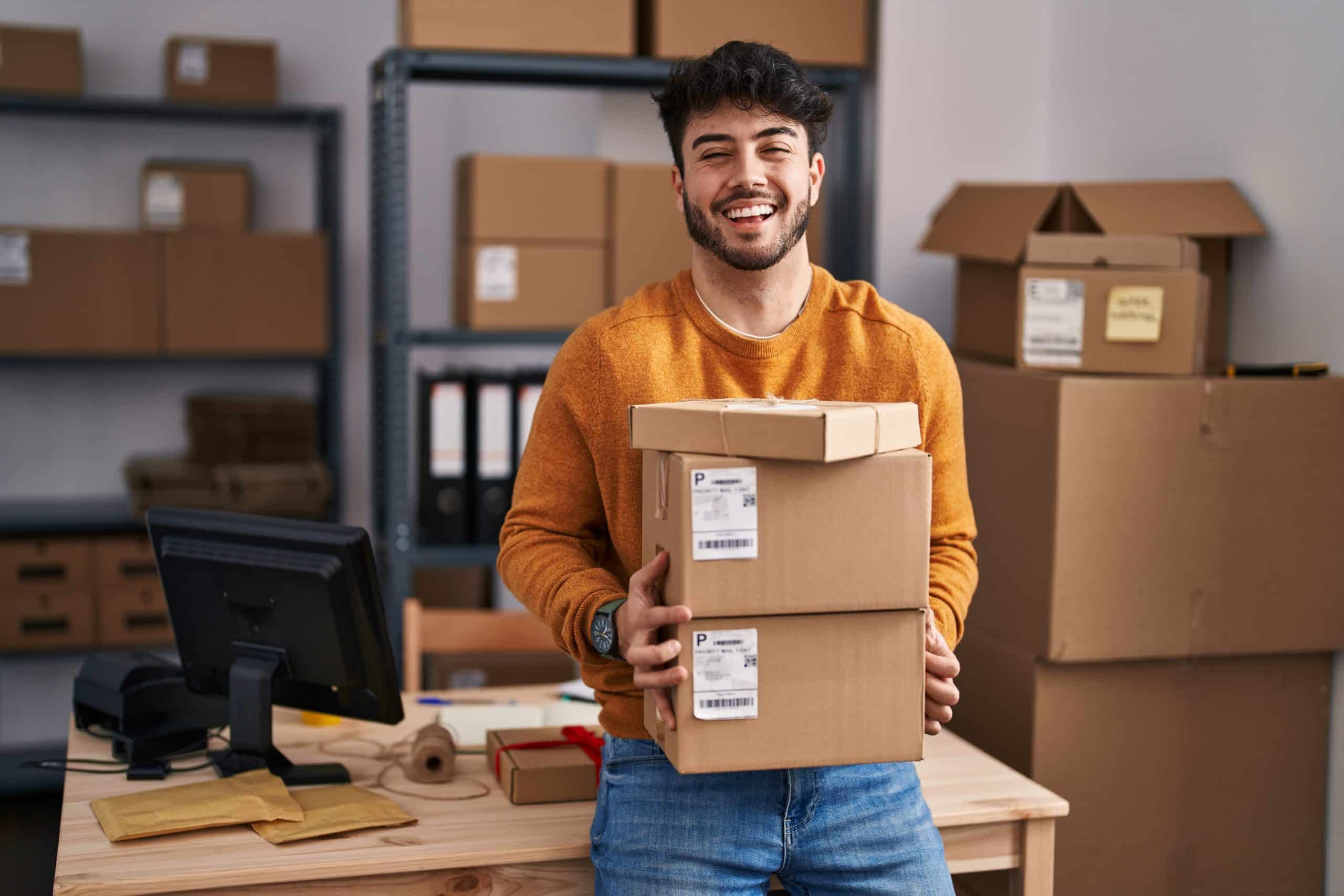 SMS Marketing - Hispanic man with beard working at small business ecommerce holding packages celebrating crazy and amazed for success with open eyes screaming excited.