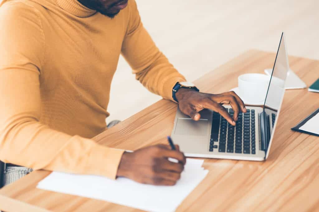 Man at work on a laptop, taking notes with paper.