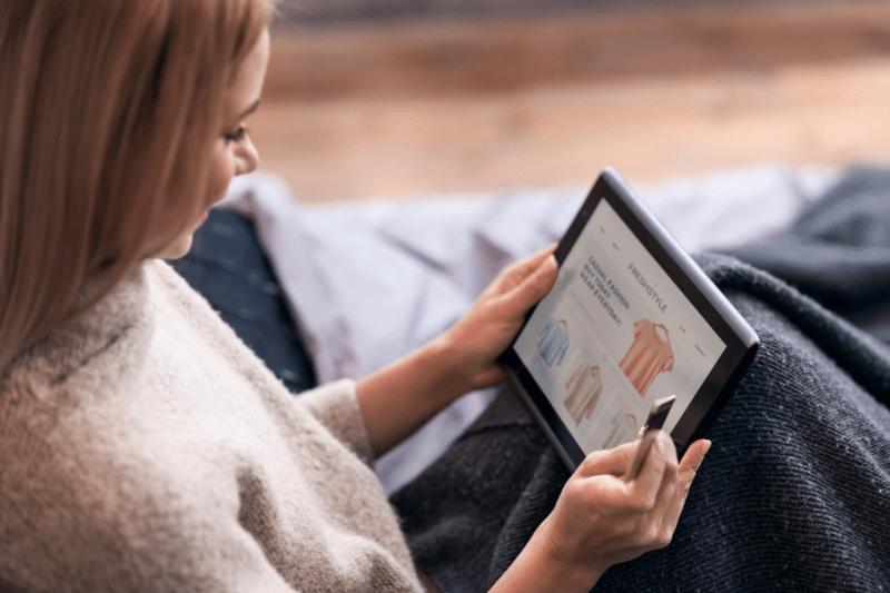 Joyful woman enjoying online shopping in bed